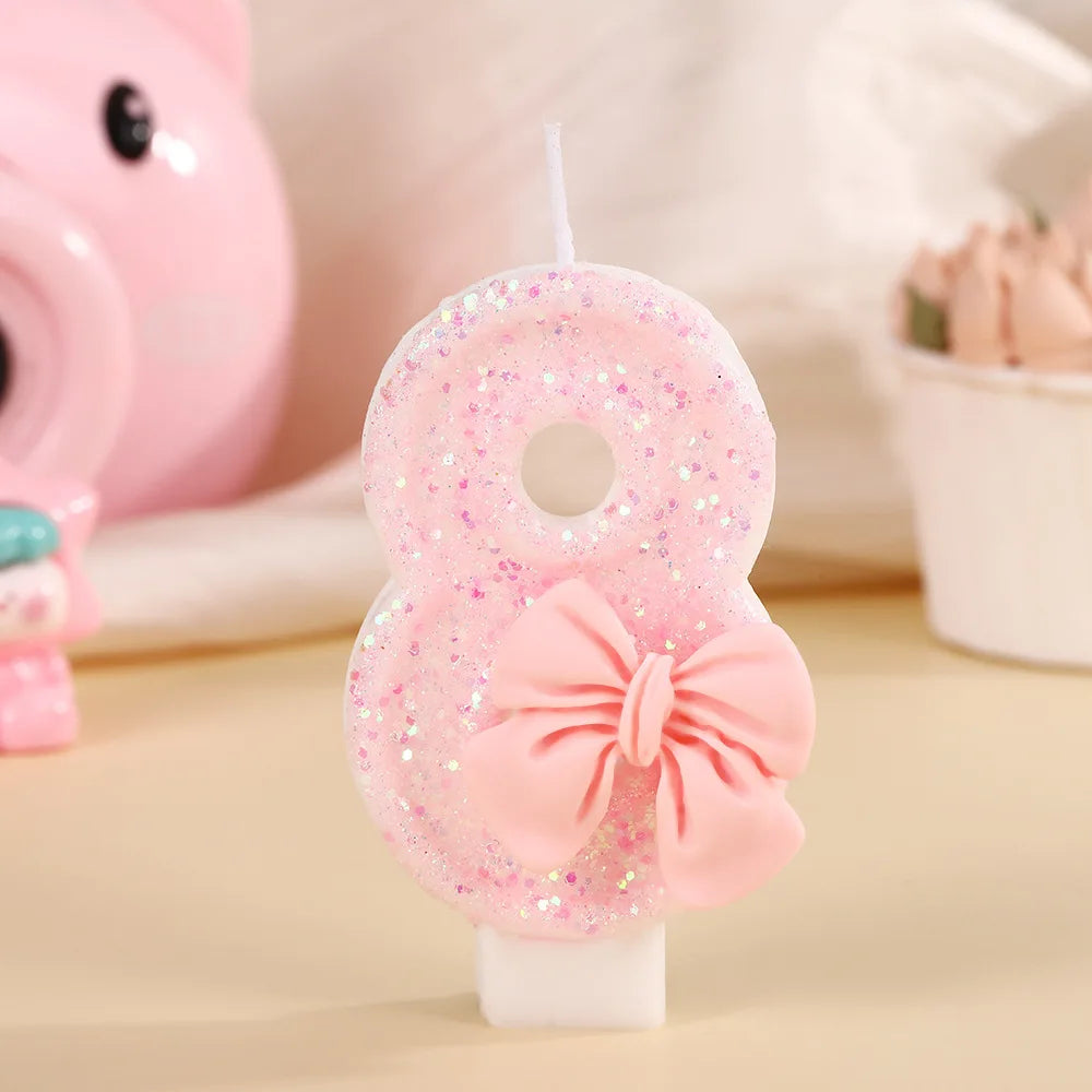 A pink glittery number eight birthday candle with a bow on a white stick, set against a soft background.