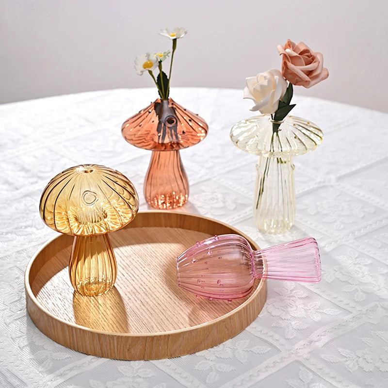 Un ensemble de vases décoratifs en forme de champignons en verre, dans des tons rose et ambre, présentés sur une nappe blanch