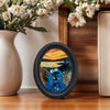 An abstract oval picture frame featuring a vibrant sunset landscape with a blue, expressive eye.
