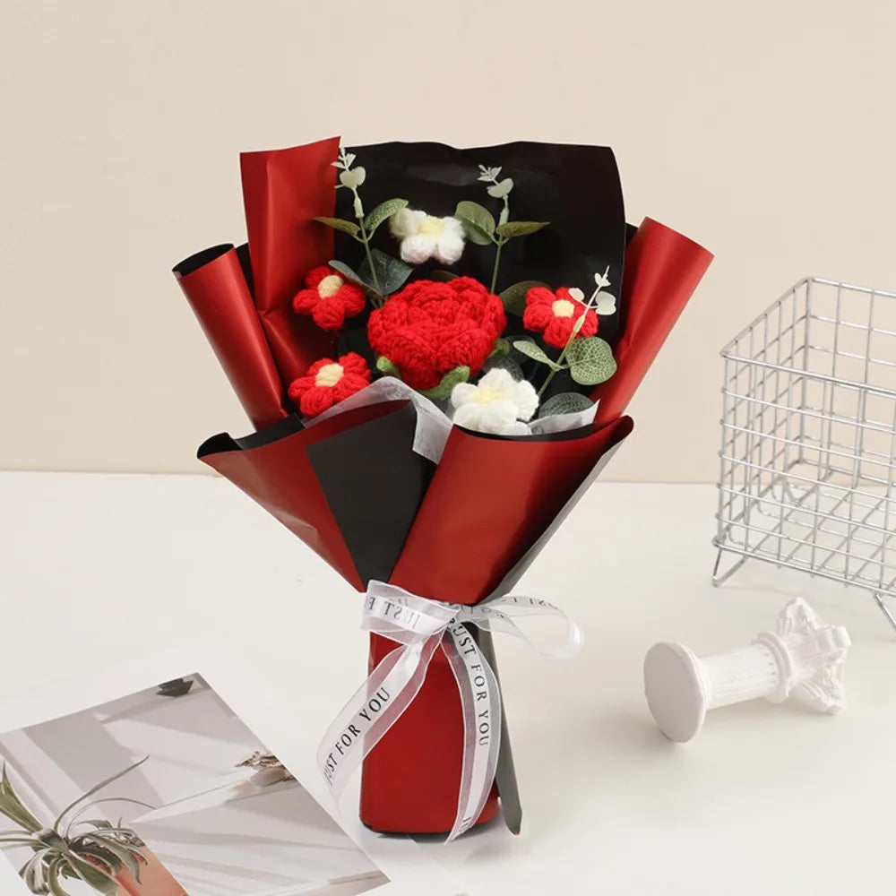 A bouquet of handmade crochet rose flowers in red and white, wrapped in dark red paper.