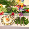 Artificial tropical palm leaves used as party decor surrounding a plate of food and floral arrangements.