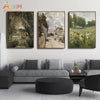 A set of three framed oil paintings depicting a vintage European countryside scene with a village and fields of wildflowers.