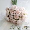 A bouquet of artificial pink peony silk flowers arranged on white paper with green stems.