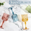 A collection of crystal wine goblets in various colors including pink, blue, and gold resting on a white marble surface.