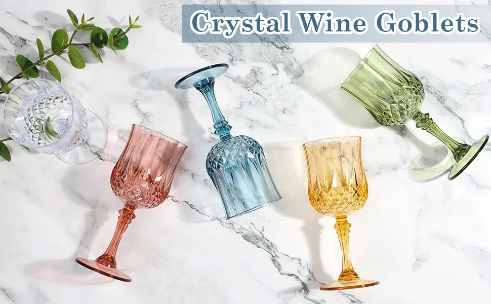 A collection of crystal wine goblets in various colors including pink, blue, and gold resting on a white marble surface.