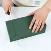 A hand is cutting a green floral foam block for party decor on a white surface.