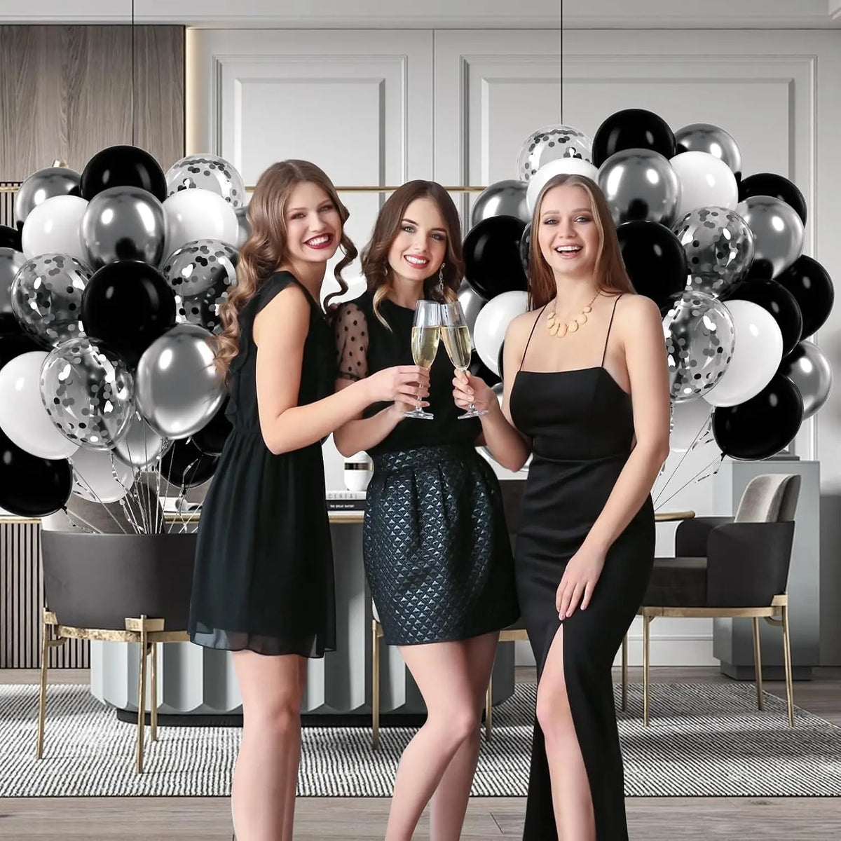 Three women in black dresses pose with silver and black balloons in a modern interior setting.