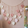 Bohemian macrame leaf wall hanging featuring various pink and cream colored leaves suspended by tassels.