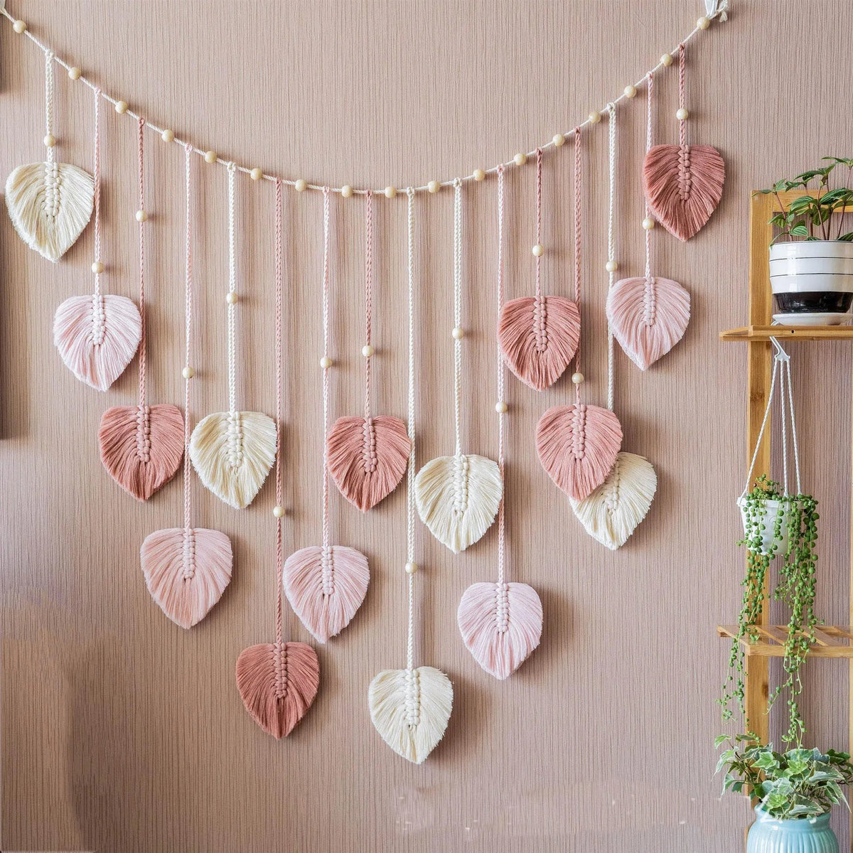 Bohemian macrame leaf wall hanging featuring various pink and cream colored leaves suspended by tassels.