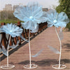 Three large light blue sheer mesh flowers on white stems displayed on a wooden walkway.