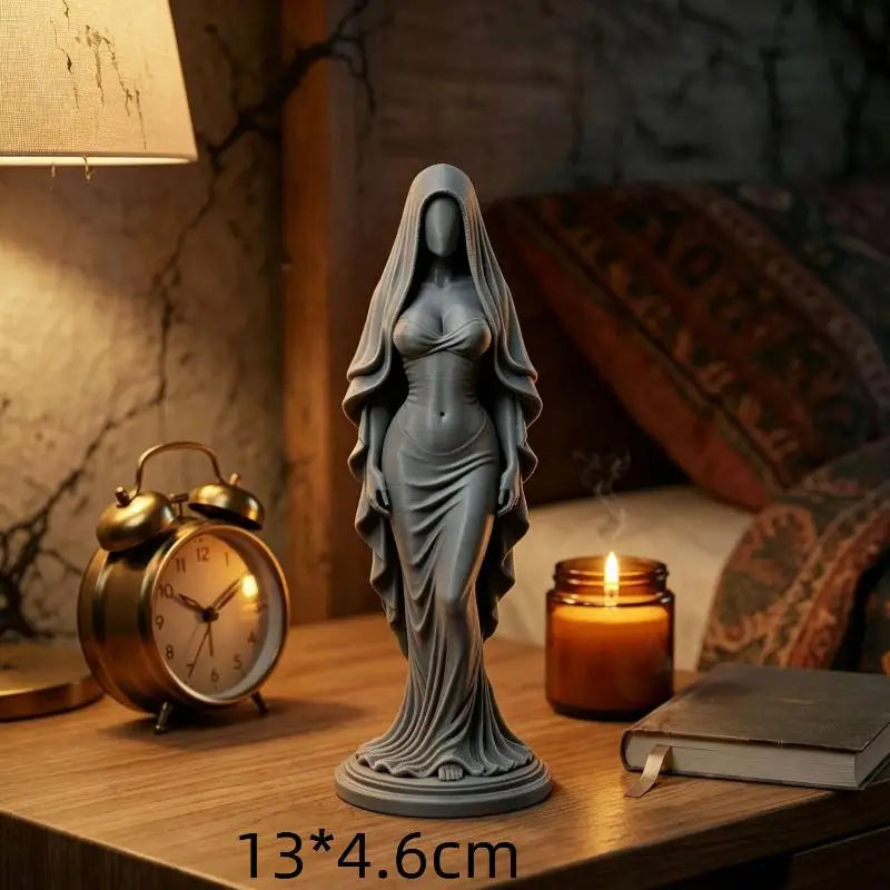 A gray praying angel figurine statue displayed on a wooden table next to a vintage gold alarm clock and a lit candle.
