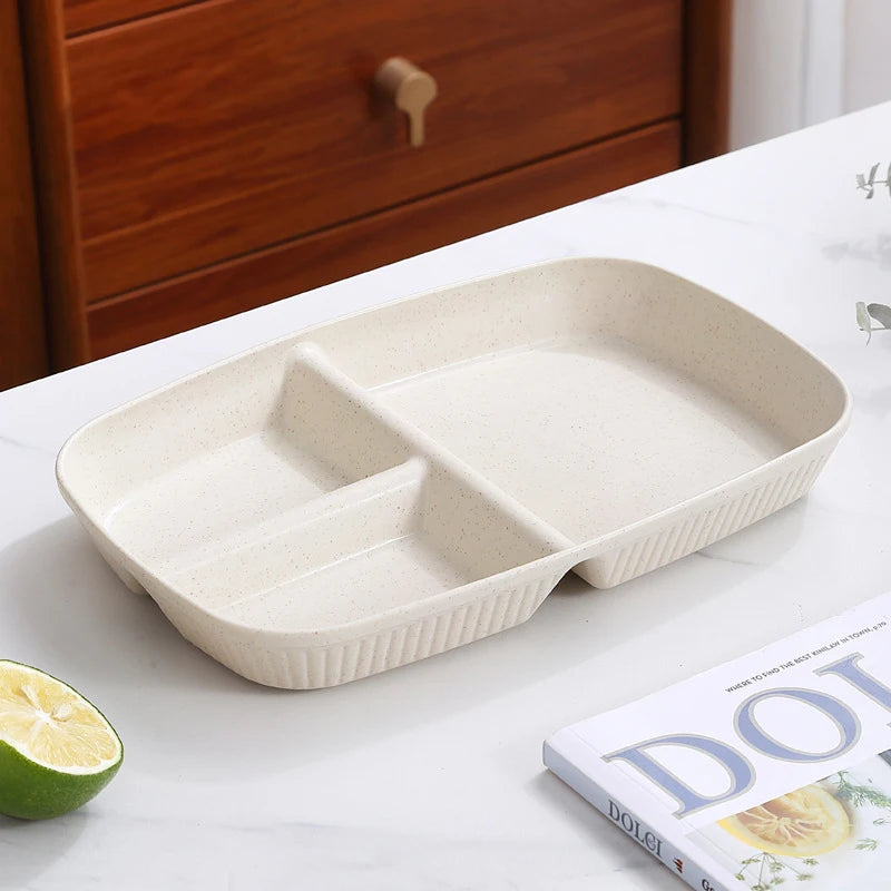 A beige 3-compartment portion control plate is displayed on a white marble surface next to a lime and a book.