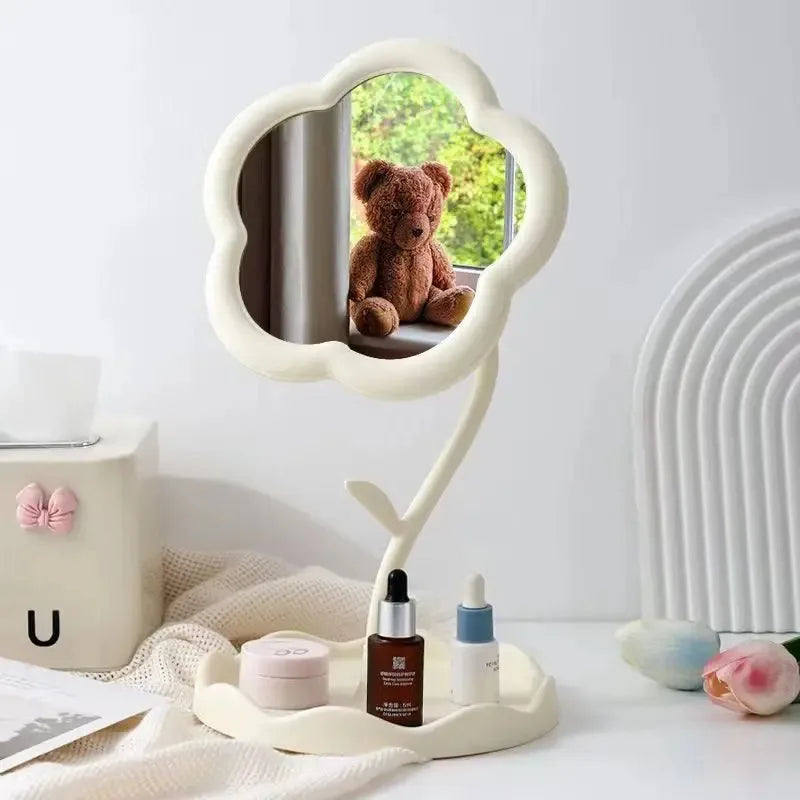 A white floral decorative mirror with a rounded frame reflects a teddy bear and is placed on a light-colored surface.