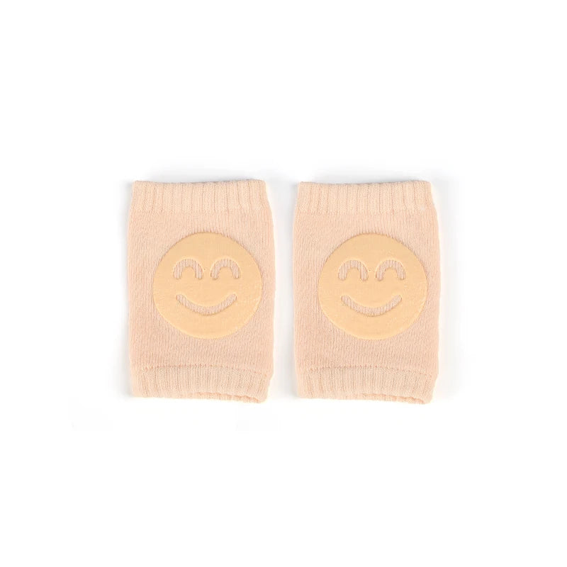 A pair of light pink knitted knee pads with yellow smiling faces for crawling infants.