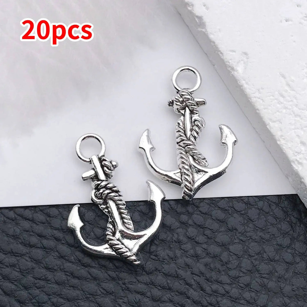 20 pieces of vintage ship anchor charms for jewelry making displayed on a black leather surface