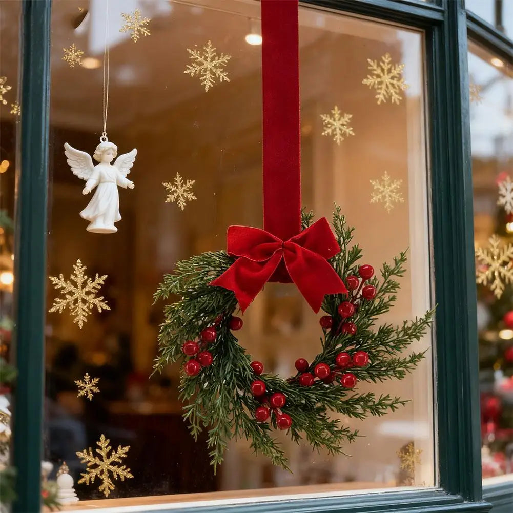 A 10-inch artificial Christmas wreath decorated with green foliage, red berries, and a large red velvet bow, displayed in a g