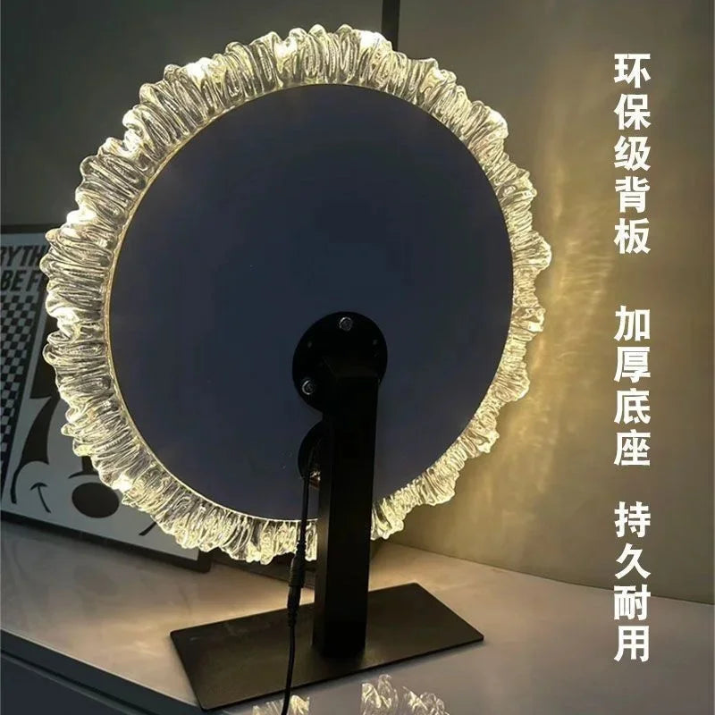 A round, textured glass vanity mirror with an illuminated frame and a stand.