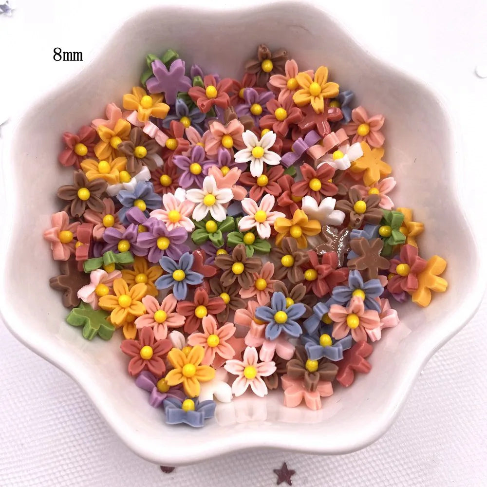 A collection of colorful 3D resin flower gems in various shades of yellow, pink, purple, and brown arranged in a white dish.