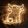 A glowing neon sign shaped like a highland cow is displayed on a dark surface.