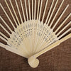 Ventilateur à main en bambou jaune clair pliable avec perforations délicates, exposé sur un tissu marron.