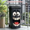 Poubelle noire décorée d'un visage de dessin animé amusant, avec des grands yeux et une bouche ouverte montrant dents et lang
