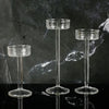 Three clear crystal glass candle holders with slender stems and wide bases displayed on a dark surface.