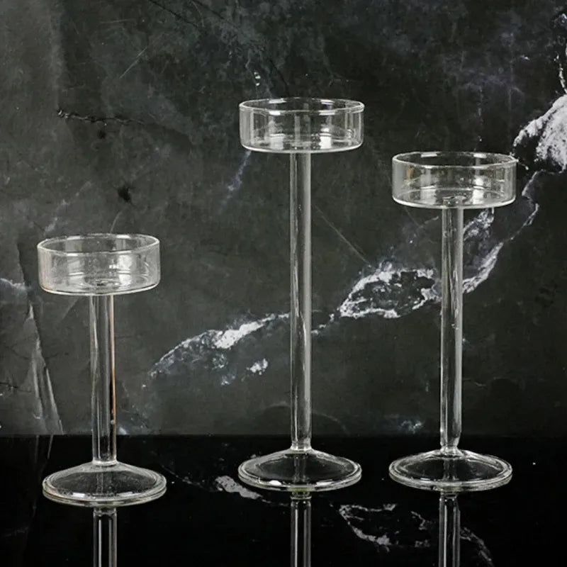 Three clear crystal glass candle holders with slender stems and wide bases displayed on a dark surface.