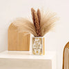 A ceramic book-shaped vase with a vintage gold finish holds dried pampas grass.
