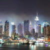 A nighttime view of the New York City skyline across the water with illuminated skyscrapers.