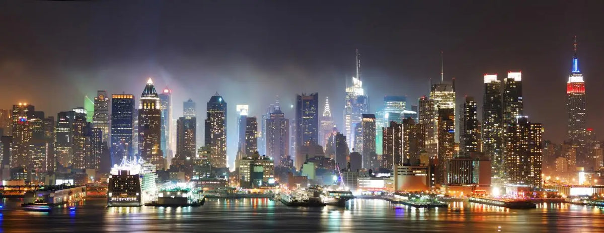 A nighttime view of the New York City skyline across the water with illuminated skyscrapers.