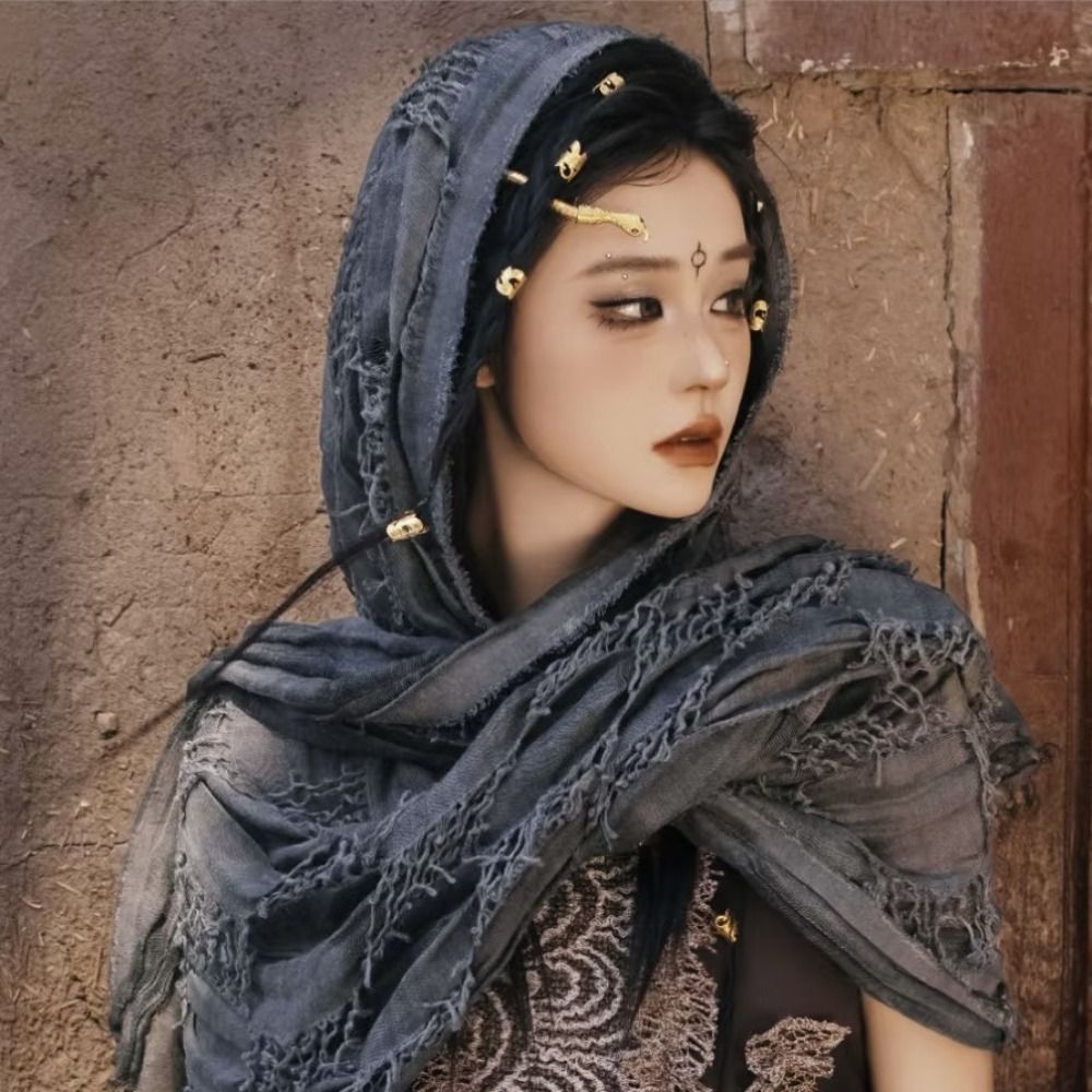 A female model wearing a dark gray hooded cloak with gold Viking-style brooches and intricate fabric.