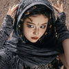 A woman wearing a dark gray hooded cloak adorned with gold Viking-style brooches.