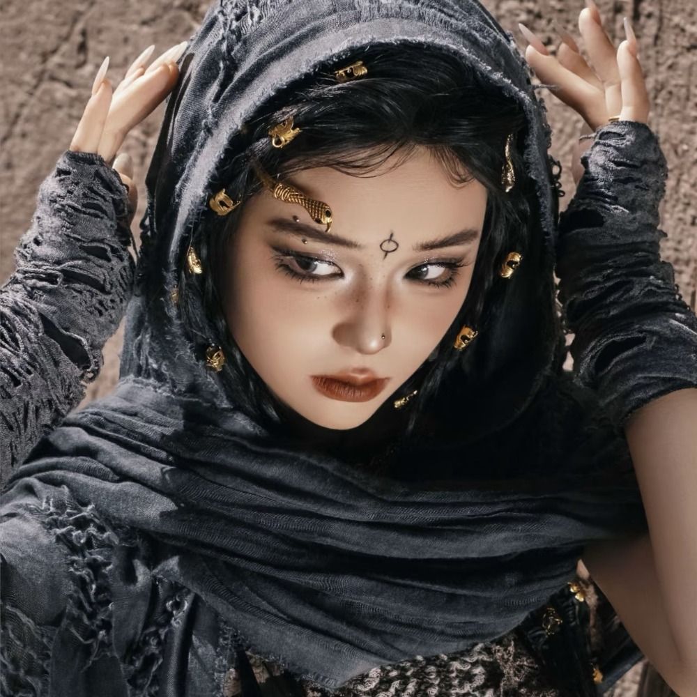 A woman wearing a dark gray hooded cloak adorned with gold Viking-style brooches.