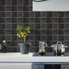 A kitchen countertop with a dark gray tiled backsplash featuring a potted olive tree and stainless steel pots.