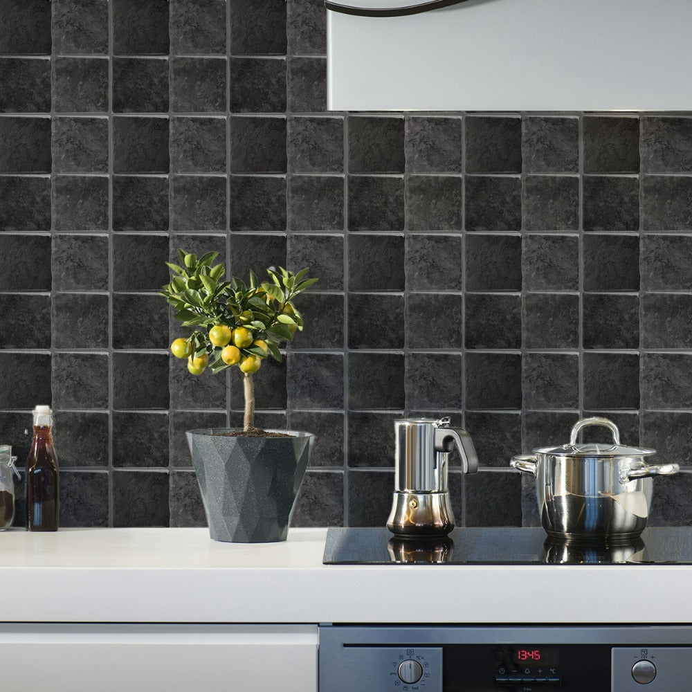A kitchen countertop with a dark gray tiled backsplash featuring a potted olive tree and stainless steel pots.