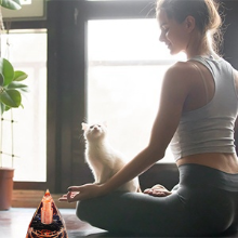 A woman sits meditating with a cat near a handmade resin orgonite pyramid featuring natural obsidian and copper coil.